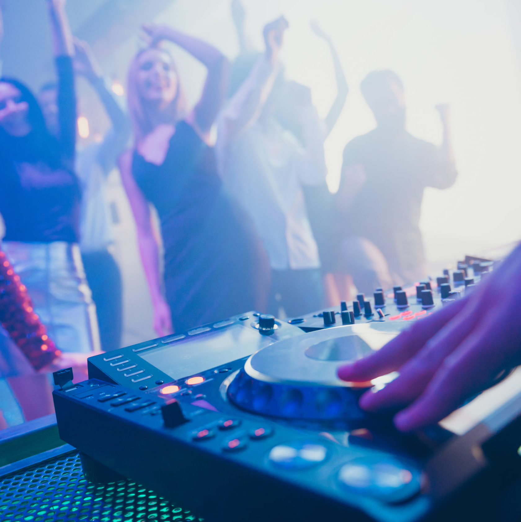 Un DJ utilise le DJ PROFESSIONNEL AVEC SONO & LUMIERES dans une boîte de nuit animée, avec des gens qui dansent et des lumières colorées en arrière-plan. L'accent est mis sur la main du DJ qui règle l'équipement professionnel au premier plan.