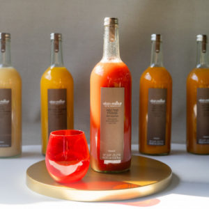 Une bouteille de 1 litre de NECTAR DE FRAISES ALAIN MILLIAT, portant une étiquette brune et un bouchon argenté, est présentée sur un plateau doré à côté d'un verre rouge, avec quatre bouteilles de mélange de jus de fruits à l'arrière-plan.