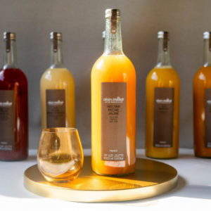 Un verre et une bouteille de NECTAR DE POIRE ALAIN MILLIAT 1L sont posés sur un plateau rond et doré, avec quatre autres bouteilles de nectar de fruits en arrière-plan.