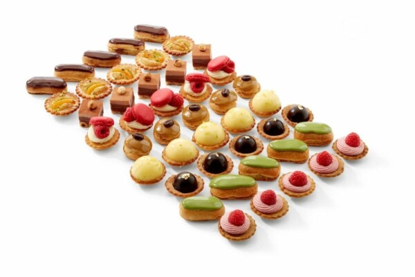 Le PETIT COCKTAIL MAGNOLIA comprend 18 pièces salées et sucrées, dont des éclairs colorés, des tartes, des macarons et des mini gâteaux garnis de chocolat, de fruits et de glaçage, le tout soigneusement disposé sur un fond blanc.