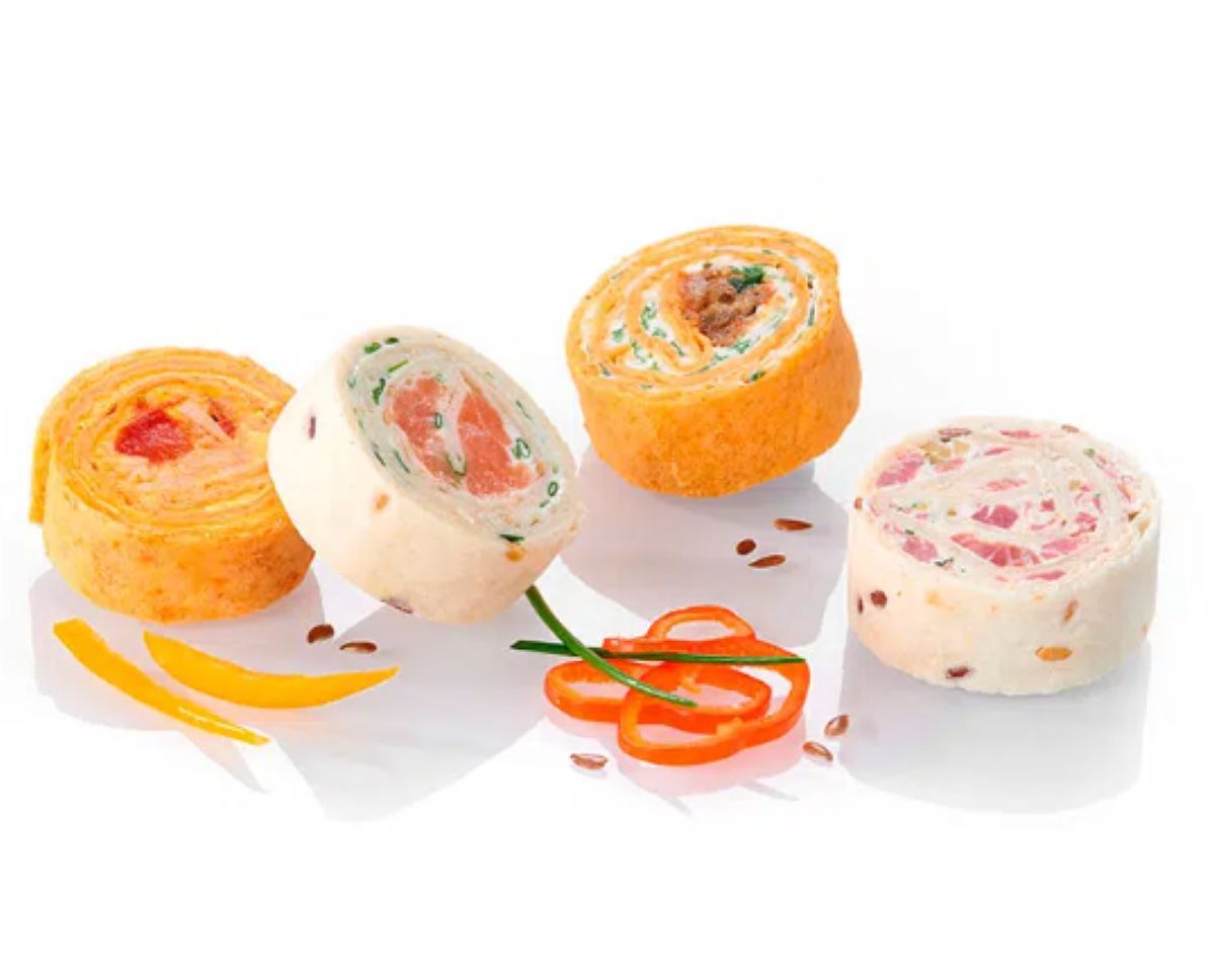 Un assortiment de 48 mini wraps du PLATEAU DE 48 MINI WRAPS est joliment disposé sur une surface blanche, garni de tranches de poivrons, de ciboulette et d'un filet de sauce jaune.