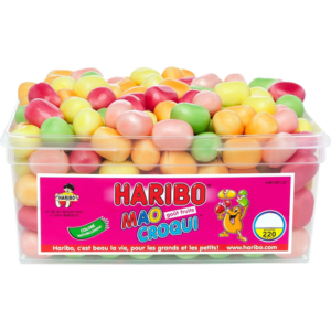 Une barquette en plastique transparent contient des bonbons aux fruits HARIBO WORLD MIX de forme ovale et colorée. L'étiquette rose affiche le logo Haribo, des personnages de dessins animés et des informations détaillées sur le produit en français.