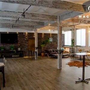 LE JAZZ HARMONY (75011) est un lieu d'événement spacieux et moderne avec des planchers en bois, des poutres apparentes, des tables mixtes et des sièges de salon, des plantes, de grandes fenêtres et une télévision sur un mur texturé ; le logo Magnolia For Event se trouve dans le coin.
