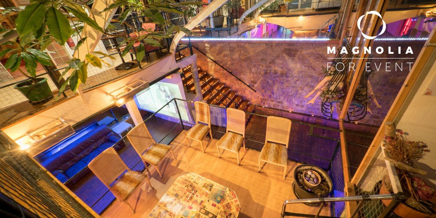 LE LOFT DE TITO (75011) propose un espace événementiel moderne avec des balcons élégants, des éclairages décoratifs, des plantes et un escalier ; le nom du lieu figure dans l'angle.