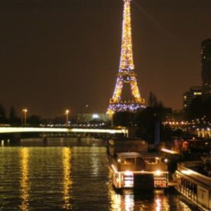 LE PETIT MISSISSIPI (75015) brille la nuit, ses lumières se reflétant dans la Seine, à côté des bateaux et des illuminations de la ville, le long des quais de Paris.