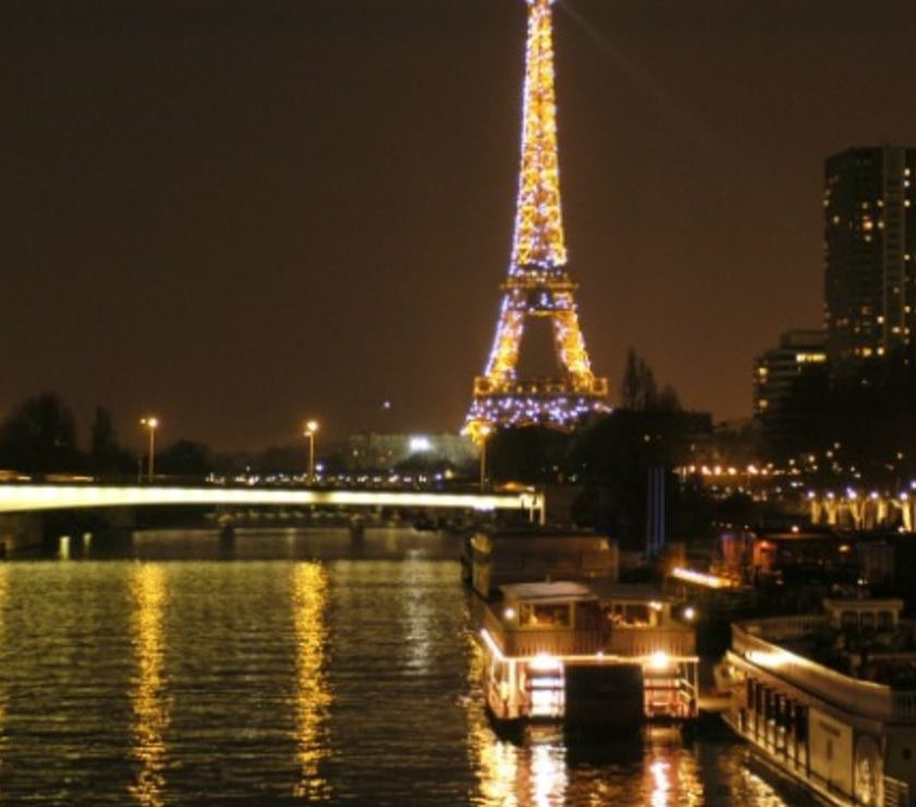 LE PETIT MISSISSIPI (75015) brille la nuit, ses lumières se reflétant dans la Seine, à côté des bateaux et des illuminations de la ville, le long des quais de Paris.