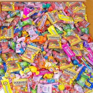 L'ASSORTIMENT DE 600 BONBONS (3,6 Kg) est une grande boîte contenant 600 bonbons mélangés, avec des emballages colorés et une variété de bonbons comme des gommes, des bonbons durs et des sucettes, le tout dans un assortiment vibrant.