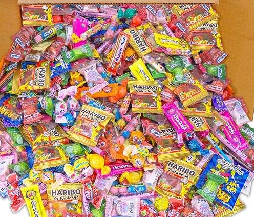 L'ASSORTIMENT DE 600 BONBONS (3,6 Kg) est une grande boîte contenant 600 bonbons mélangés, avec des emballages colorés et une variété de bonbons comme des gommes, des bonbons durs et des sucettes, le tout dans un assortiment vibrant.