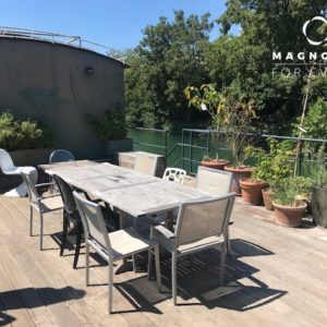 Terrasse extérieure en bois avec une longue table et des chaises dépareillées, entourée de plantes en pot et bordée d'arbres et d'une balustrade en métal, mettant en vedette LA PÉNICHE DE JEROME (92040). Le logo Magnolia For Event se trouve dans le coin supérieur droit.
