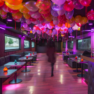 À LA BELLE PÉNICHE (75005), on déambule dans un salon animé, baigné de lumière rose, avec des ballons colorés au plafond, des petites tables et des banquettes rembourrées le long des murs.