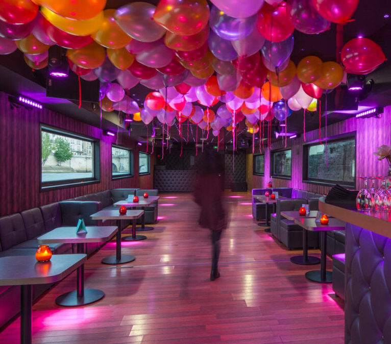 À LA BELLE PÉNICHE (75005), on déambule dans un salon animé, baigné de lumière rose, avec des ballons colorés au plafond, des petites tables et des banquettes rembourrées le long des murs.