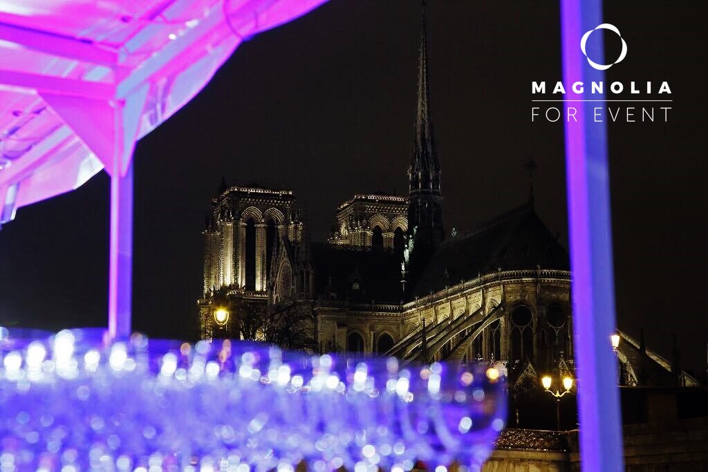 Vue nocturne de la cathédrale Notre-Dame de Paris avec, au premier plan, des tables et des verres illuminés ; logo de LA BELLE PÉNICHE (75005) dans le coin supérieur droit.