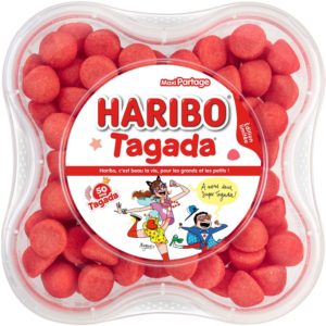 Un récipient en plastique transparent contenant des bonbons à la fraise FRAISES TAGADA (1 kg) avec une étiquette colorée comportant des illustrations ludiques, un texte en français et des bonbons ronds rouges visibles à l'intérieur.