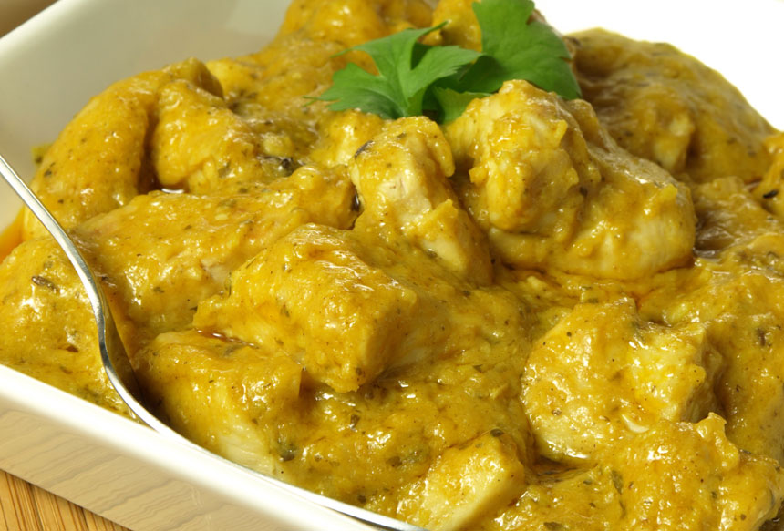 Gros plan sur un bol de COLOMBO DE POULET (300g la part), un curry de poulet jaune crémeux, garni de coriandre fraîche et servi avec une cuillère.