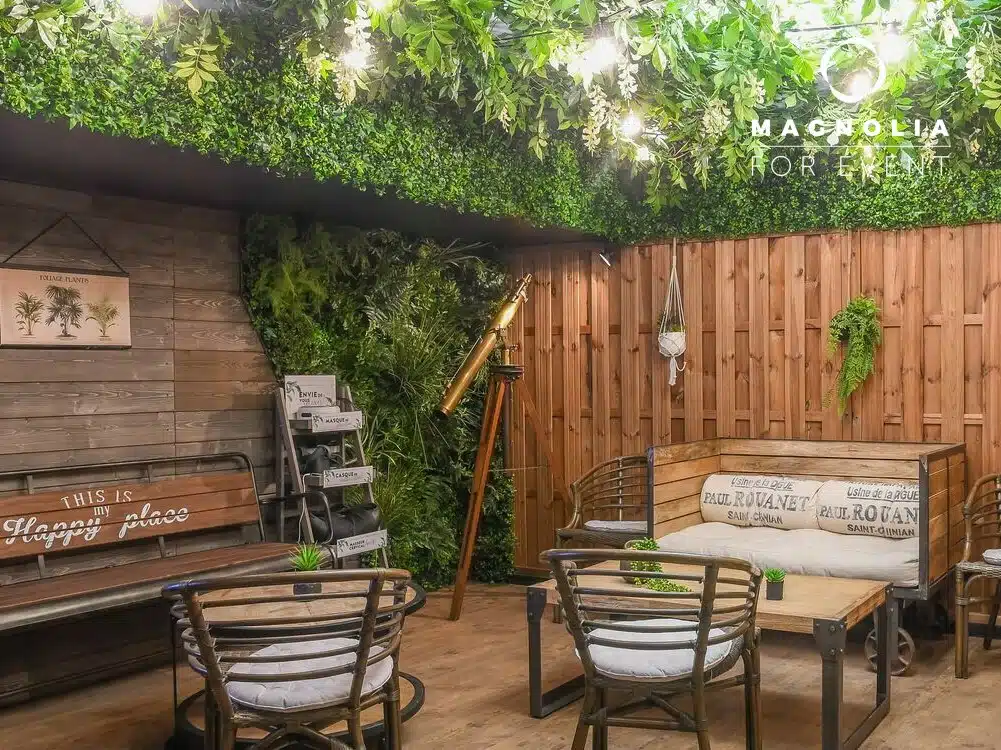 LE COSY CHIC dispose d'un patio intérieur confortable avec des meubles en bois, de la verdure luxuriante, un éclairage chaleureux, un télescope, des coussins décoratifs et des panneaux pour une atmosphère relaxante inspirée de la nature.