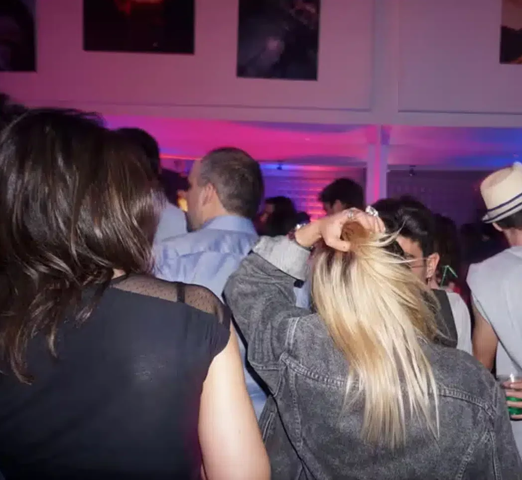 Les invités se mêlent au LOFT MONTMARTRE (75018) sous des lumières violettes et roses vibrantes. La plupart tournent le dos à l'appareil photo, tandis qu'une femme blonde se touche la tête, profitant de l'atmosphère animée de l'intérieur.