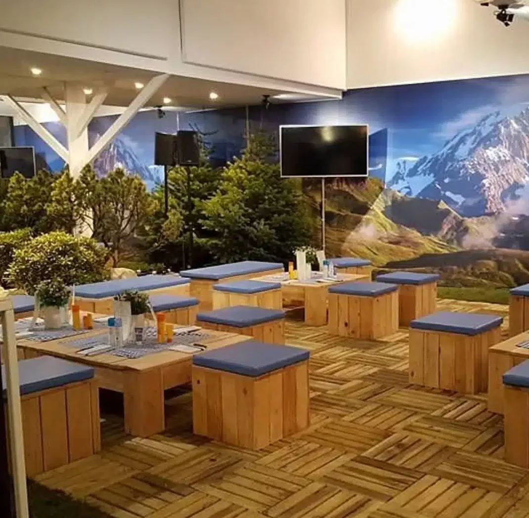 LE LOFT MONTMARTRE (75018) offre un cadre intérieur moderne avec des tables en bois, des bancs à coussins bleus, de la fausse verdure et une fresque de montagnes enneigées pour un pique-nique en plein air.