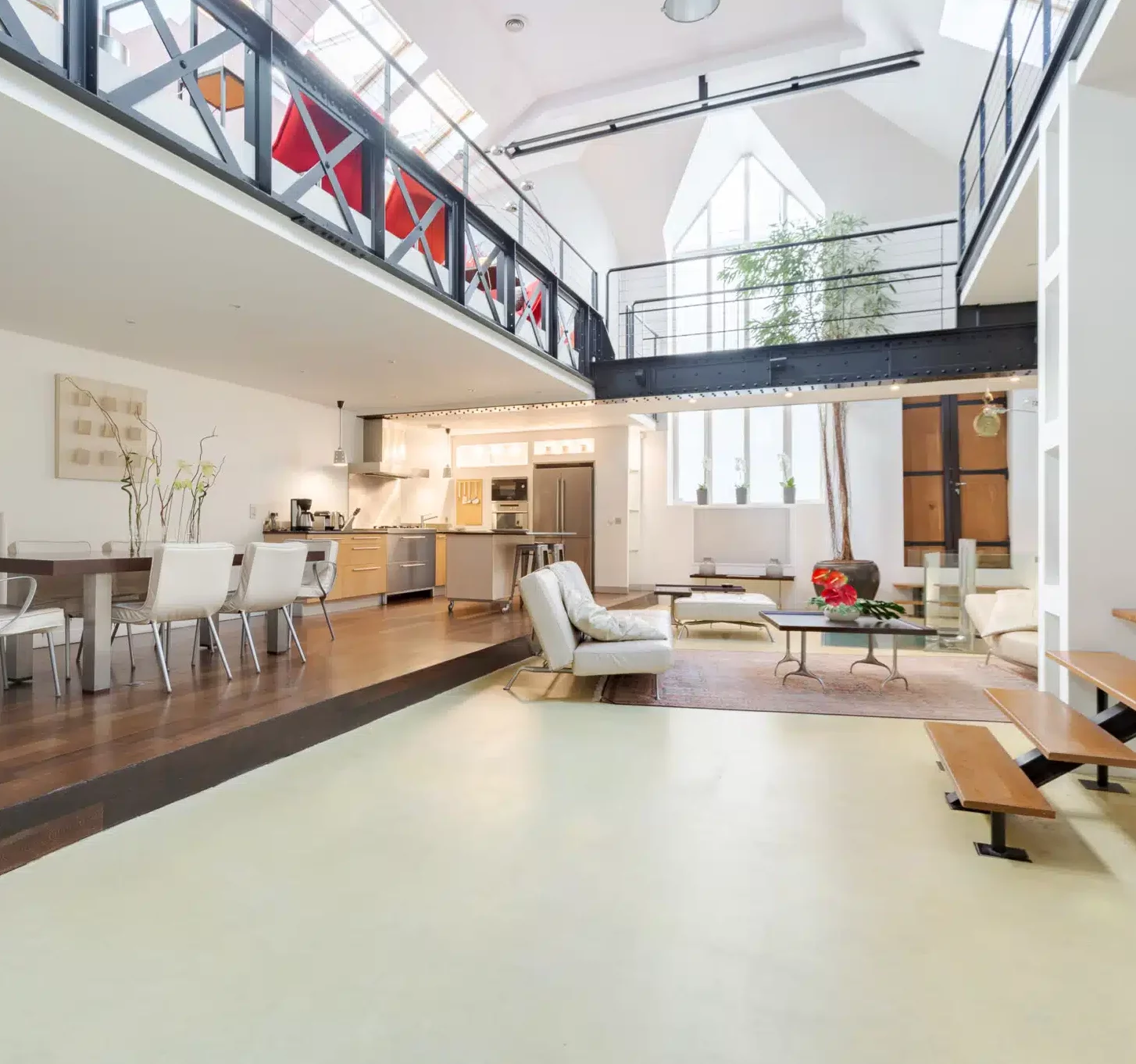 LE LOFT FACTORY (75002) propose un loft spacieux et moderne avec de hauts plafonds, de grandes fenêtres, une mezzanine, des espaces cuisine/salle à manger/salon ouverts avec des meubles contemporains, des plantes d'intérieur, un décor minimaliste et une lumière naturelle abondante.