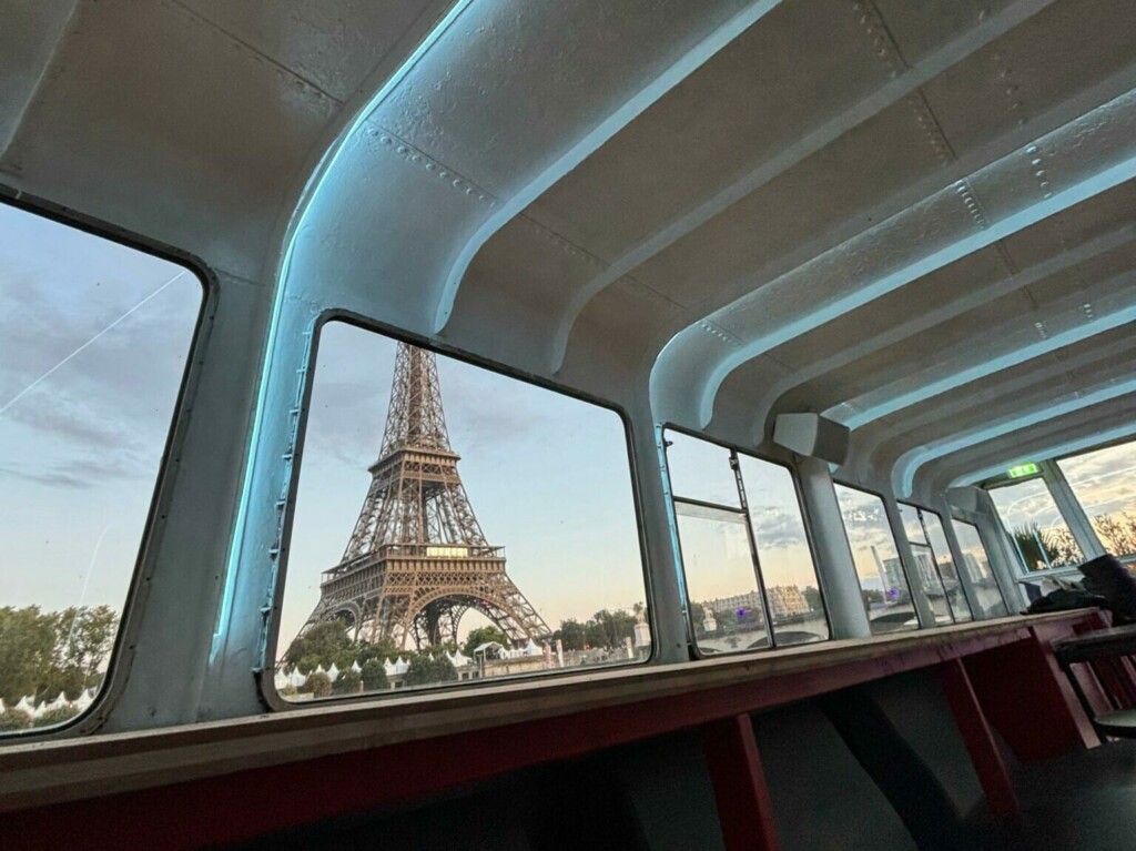 La Tour Eiffel vue à travers de grandes fenêtres à l'intérieur de LA PÉNICHE CROISIÈRES DE BERCY (75013), avec un plafond futuriste et une vue en angle du coucher de soleil sur l'emblème de Paris.