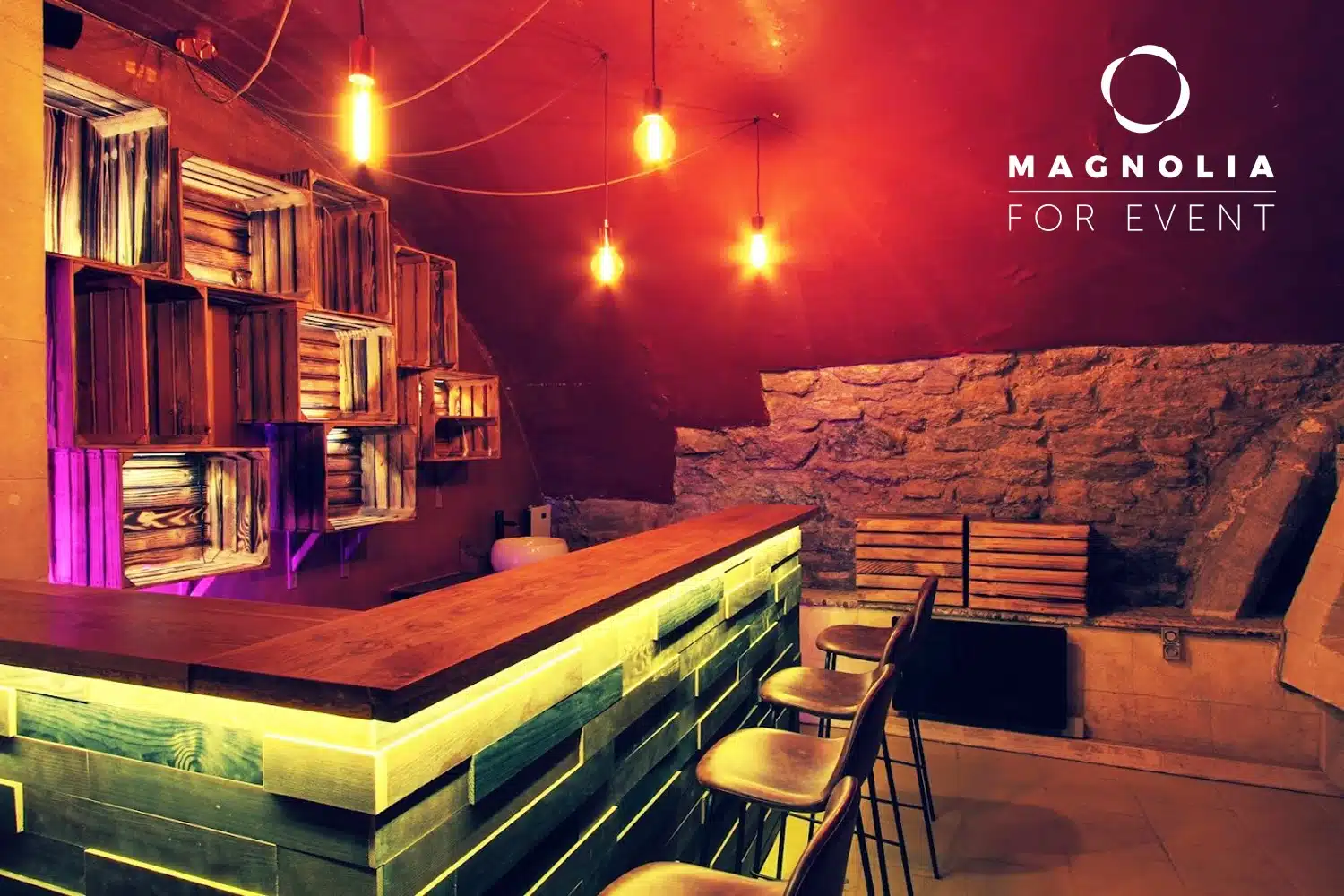 LE PETIT PARIS CACHÉ (75004) présente un bar élégant avec des lumières jaunes, des tabourets en bois, un mur en pierre et des étagères en cagettes. Le plafond rouge ajoute une touche d'élégance, avec le logo MAGNOLIA FOR EVENT affiché dans le coin supérieur droit.