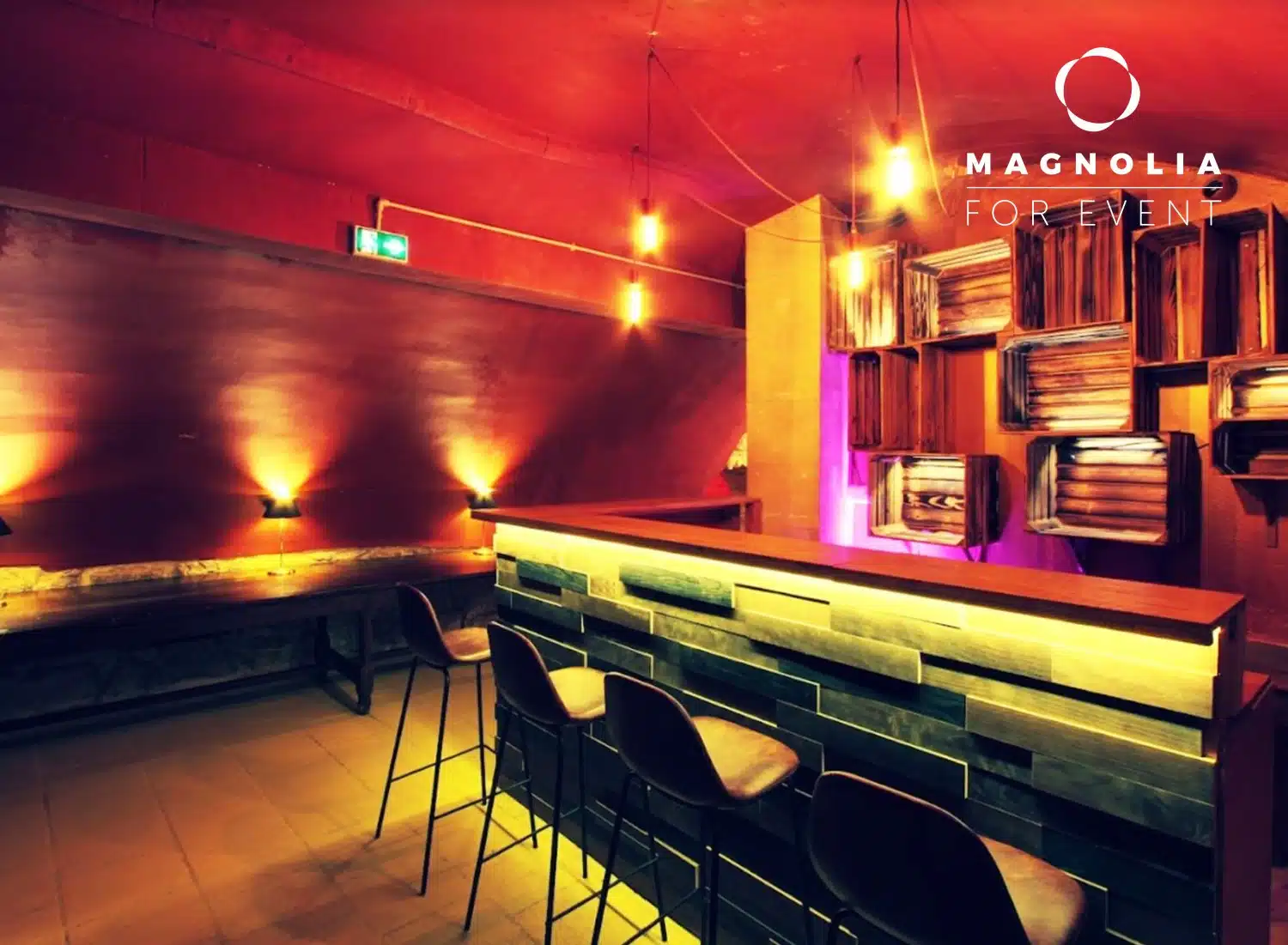LE PETIT PARIS CACHÉ (75004) dispose d'un bar moderne avec un comptoir en bois, trois tabourets de bar noirs, un éclairage chaleureux, des œuvres d'art murales abstraites et une ambiance chaleureuse et accueillante. Le logo Magnolia For Event se trouve dans le coin supérieur droit.