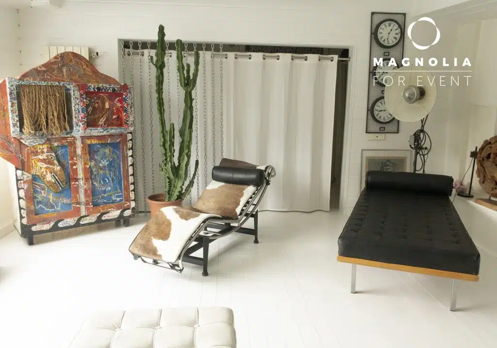 Une pièce moderne et lumineuse avec des sols blancs, un cactus, deux chaises longues (dont une avec des coussins en peau de vache), une armoire peinte de façon abstraite, une lampe d'atelier et deux horloges murales. Le logo de LA PÉNICHE SÉRÉNITÉ (92390) apparaît dans le coin supérieur droit.