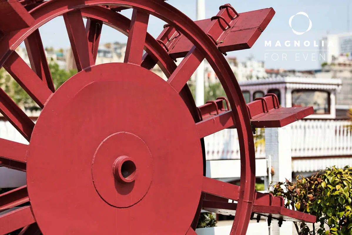 Gros plan d'une grande roue à aubes rouge sur un bateau fluvial, les bâtiments de la ville étant flous derrière. Le texte blanc sur l'image indique LE NASHVILLE TENNESSE (75015).