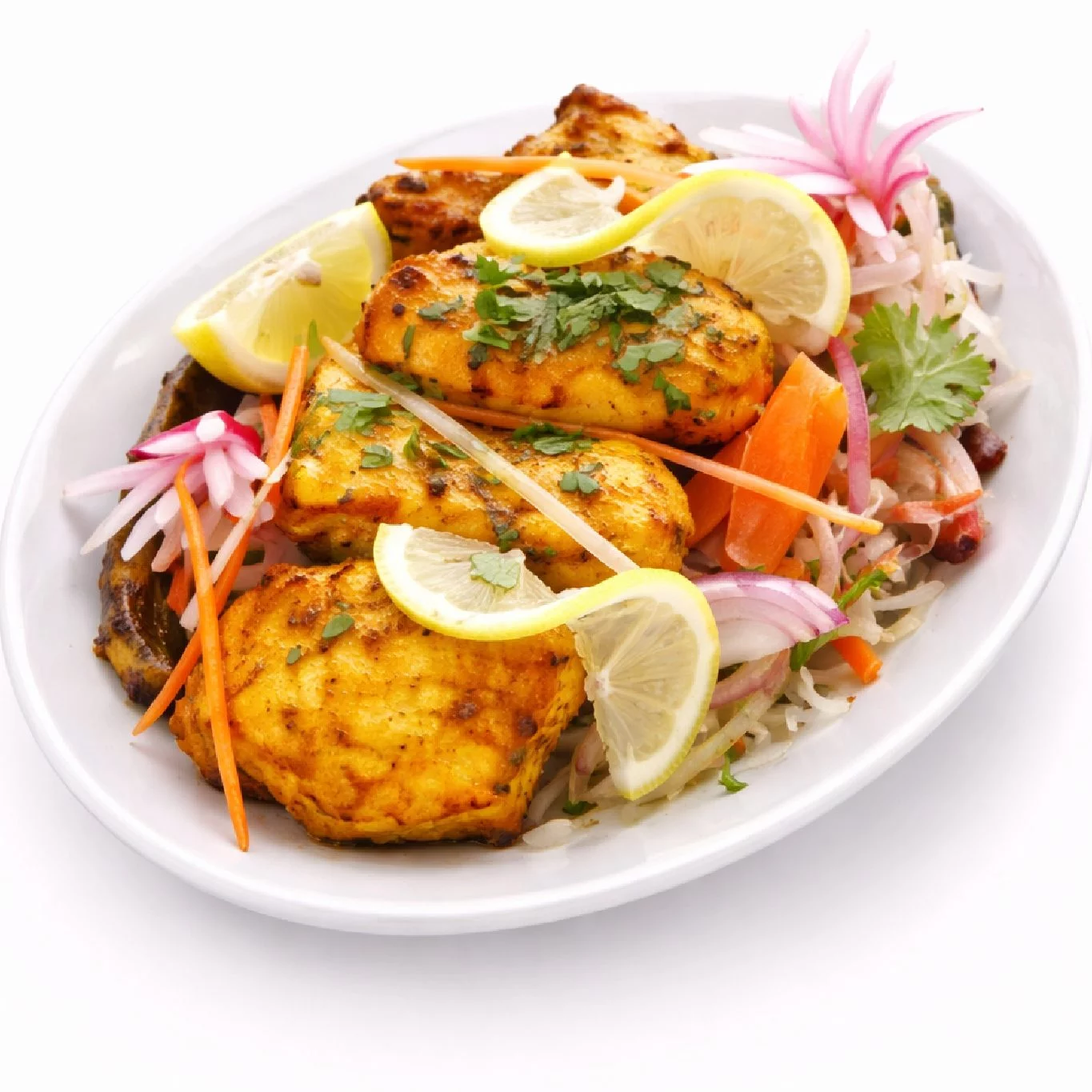 BOLYWOOD KEBAB (300g) : Morceaux de poulet marinés et grillés, garnis de citron et de coriandre, servis dans une assiette ovale blanche avec des oignons émincés, des carottes, des radis et une salade de chou frais.