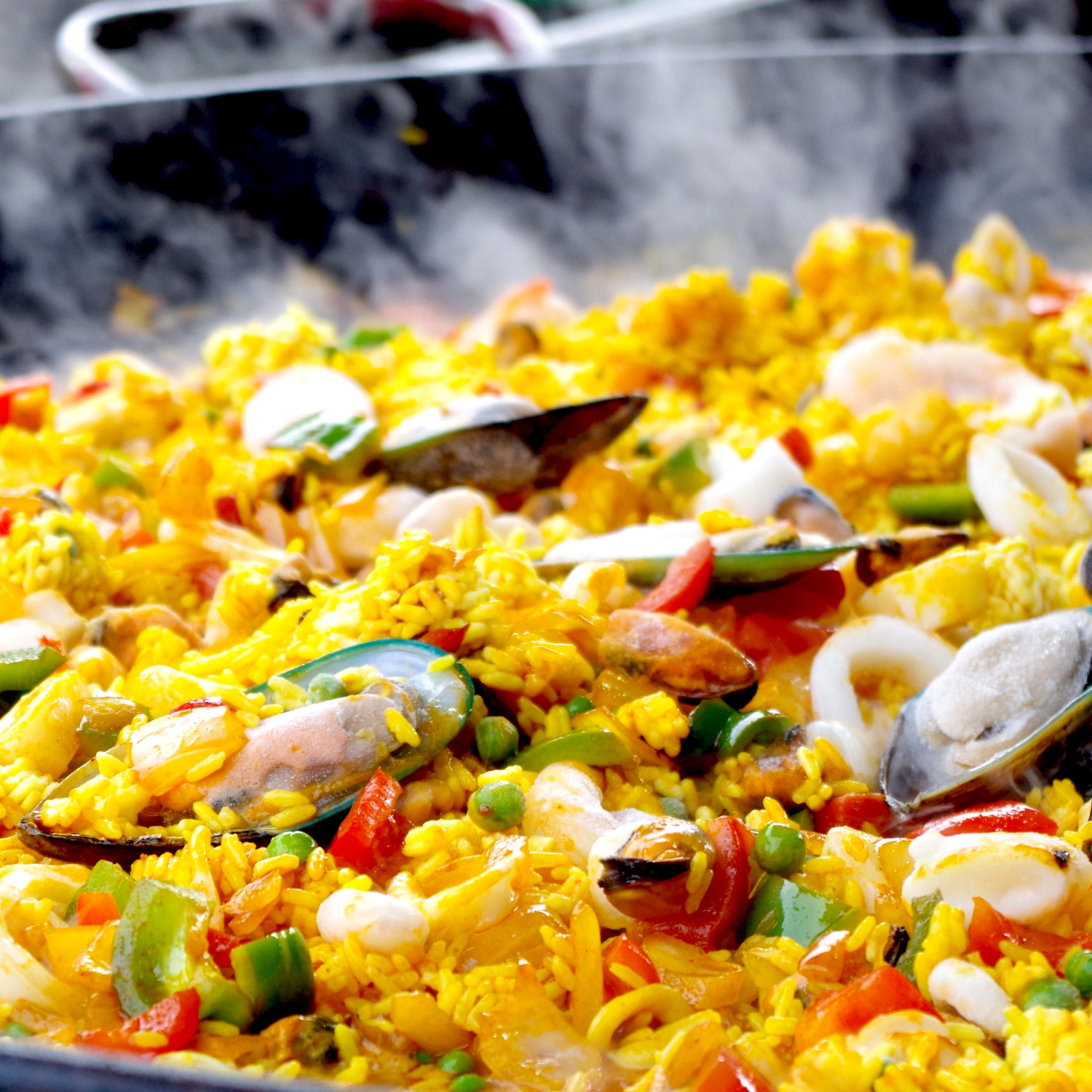 Gros plan sur la PAËLLA PARTY (400g/pers & Matériel fourni) : paella colorée aux fruits de mer avec du riz jaune, des moules, des crevettes, des petits pois et des poivrons, servie chaude comme de la vapeur et fraîchement cuite dans une grande poêle.