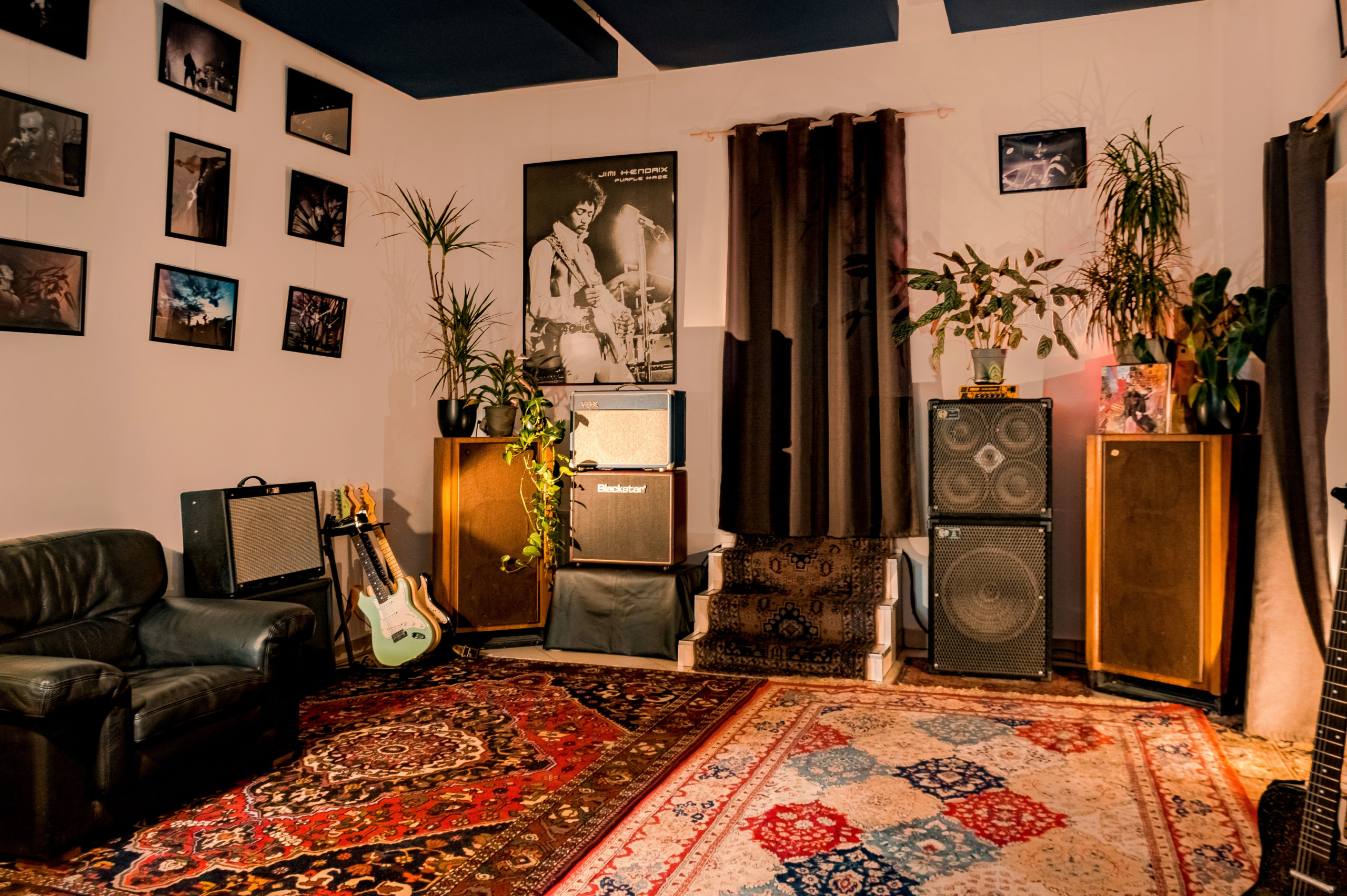 LA DEMEURE DU BOIS DE VERRIERES (92140) dispose d'une salle de musique confortable avec des tapis, des guitares, des amplificateurs, de grandes enceintes, des plantes en pot, un fauteuil noir, des photos et des affiches de musique encadrées et des fenêtres à rideaux.