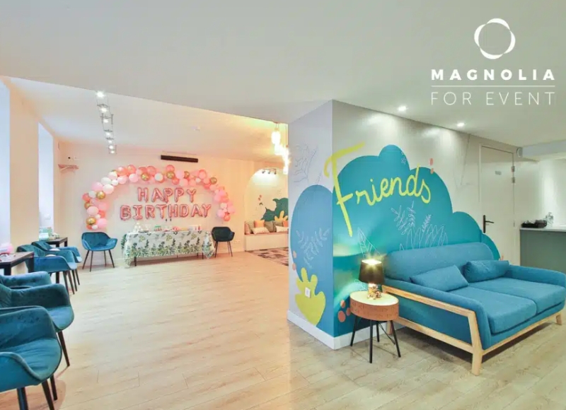 L'ESPACE DES AMIS DU 15ème (75015) est un espace lumineux décoré pour les fêtes d'anniversaire avec des ballons roses, un panneau "Happy Birthday", des chaises et des canapés bleus, ainsi qu'une fresque murale joyeuse "Friends".