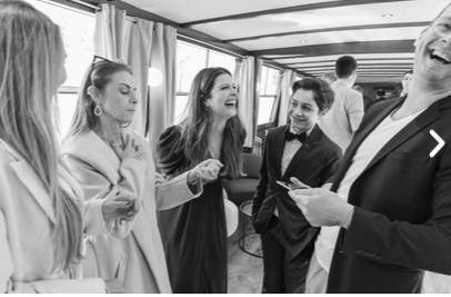 Un groupe animé en tenue semi-formelle s'amuse à l'intérieur, souriant et riant en tenant un téléphone pendant "UN MAGICIEN PROFESSIONNEL (Une performance époustouflante !)", créant une atmosphère joyeuse et vibrante.