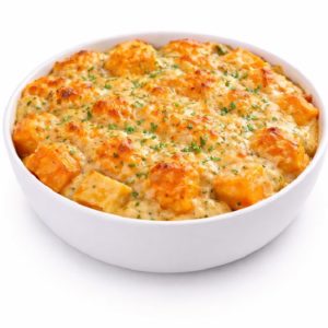 Un bol blanc contient le GRATIN D'IGNAMES (Minimum de commande 5 parts - 250g la part), un plat cuit au four garni de pâtes au fromage dorées et garni de persil frais haché.
