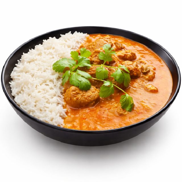 Un bol noir avec du riz blanc et du CURRY D'AGNEAU (minimum de commande 10 plats - 250g la part), garni de coriandre fraîche, sur fond blanc.